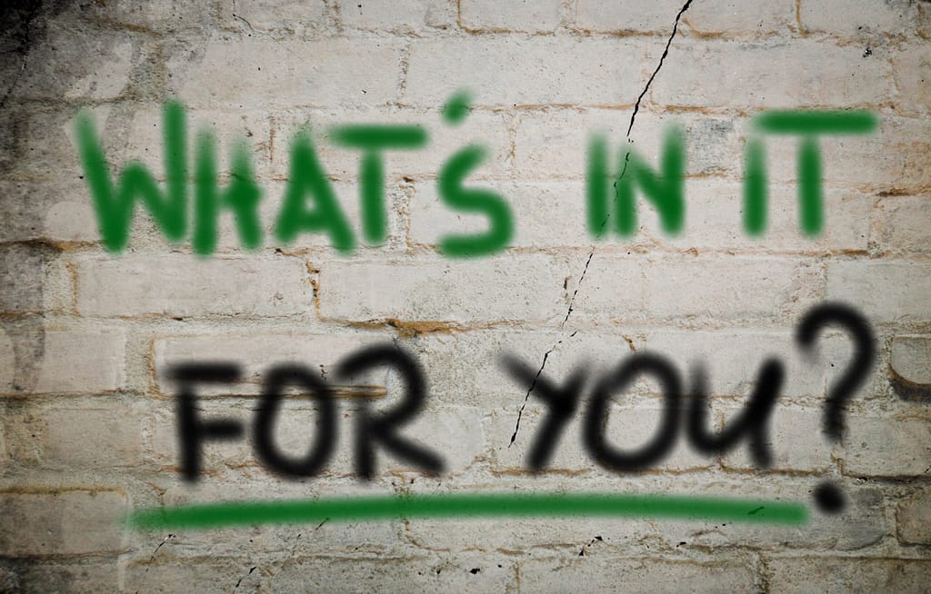 Picture of graffiti on a wall that reads, “What’s in it for you?”.