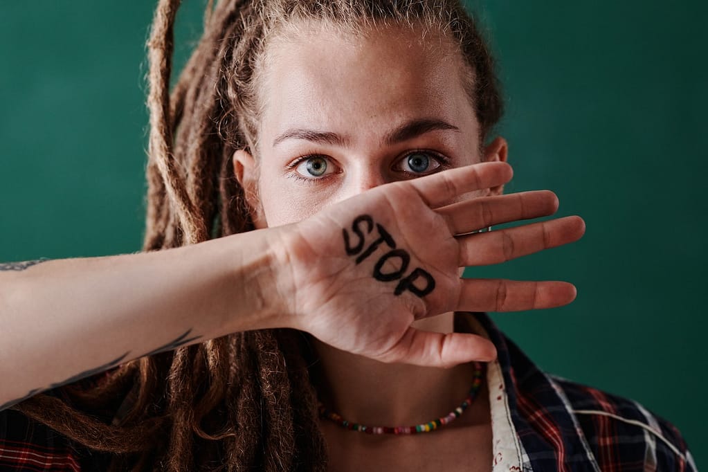 A woman holding up her hand with the word “stop” written on it.