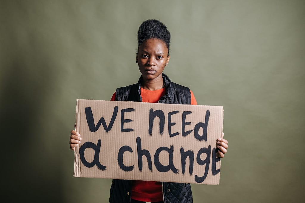 A woman holding a placard that reads we need change.