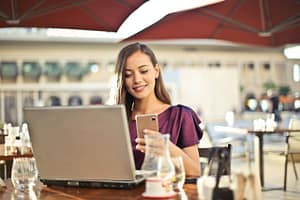 Young woman in a cafe using a smart phone and a laptop.