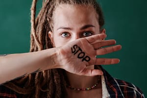 A woman holding up her hand with the word “stop” written on it.